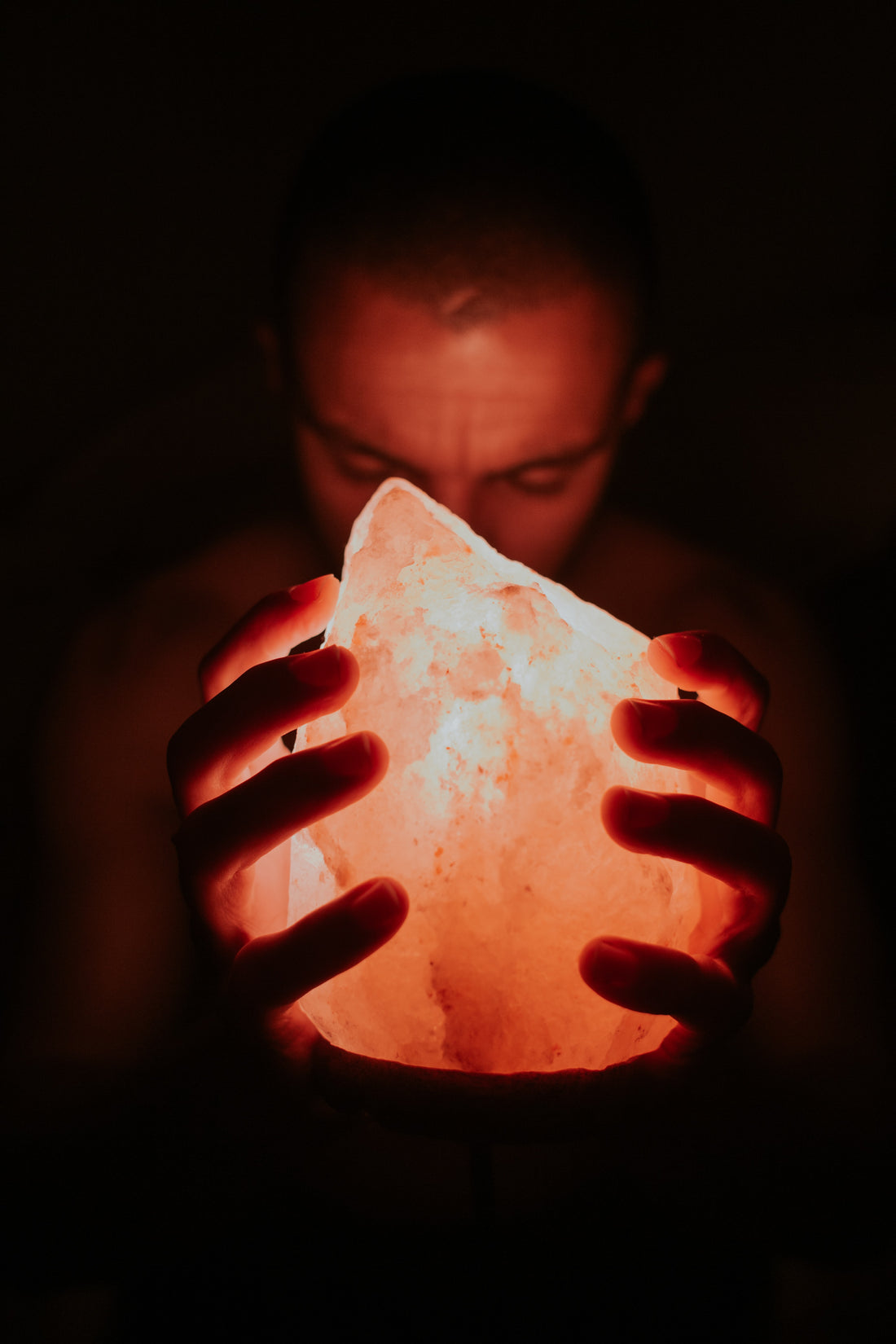 a person in a dark room holding a lit himalayan salt lamp