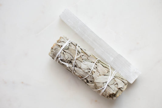 a white sage smudge stick and selenite stick next to each other